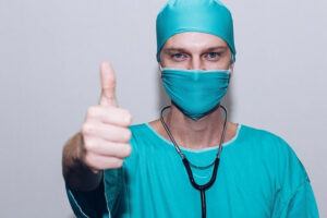 Man in blue scrubs, masked, thumbs up sign