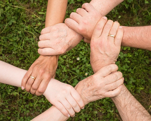 Image is of hands interlocking wrists in a ring