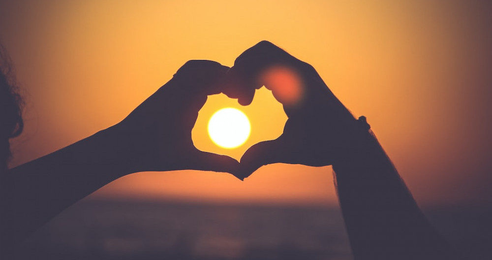 Image is of two hands making a heart around the sun