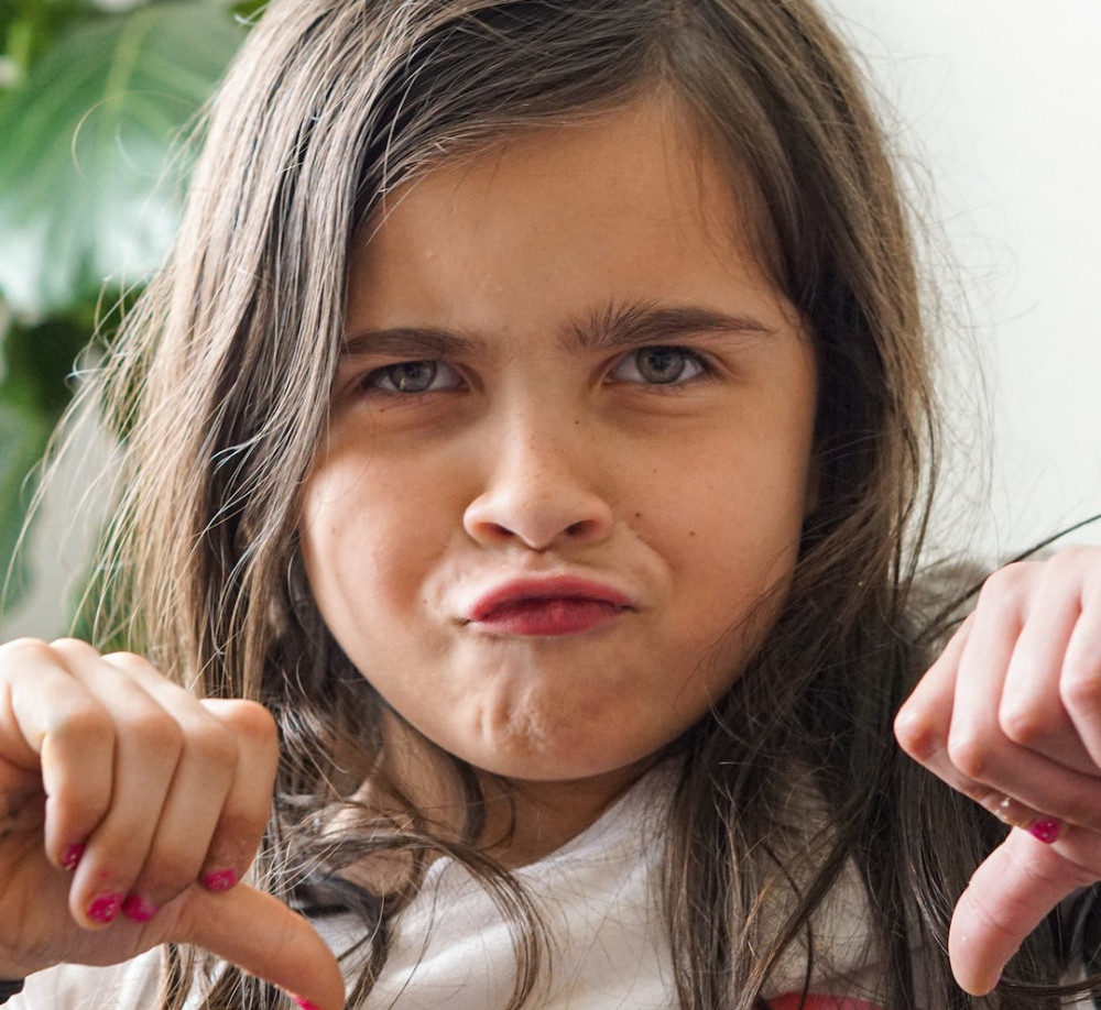 Image is of a girl with her thumbs down indicating con's